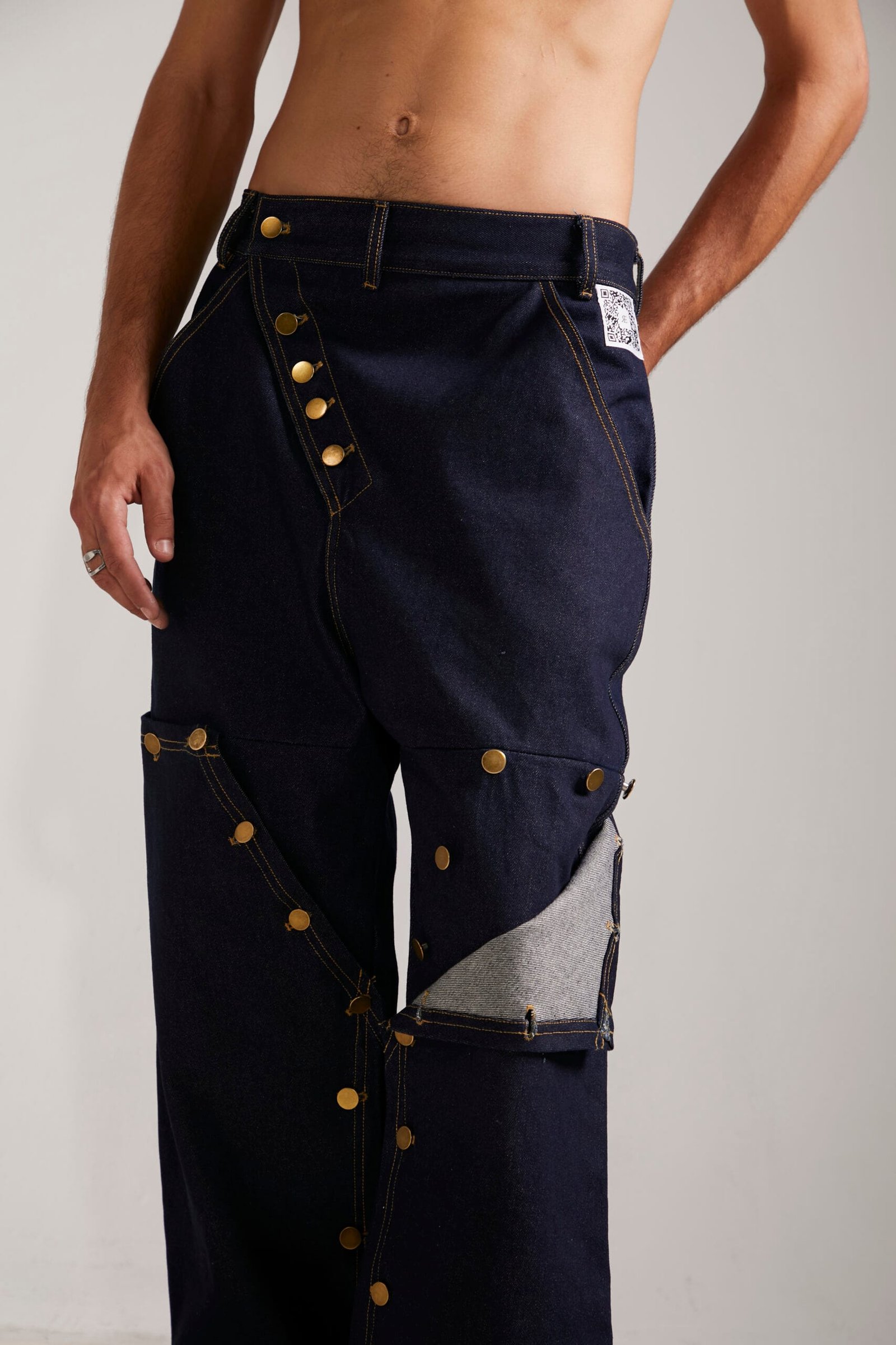 Detalle de los botones a presión y etiqueta interactiva del pantalón Utility Jeans, destacando como referente en marcas de ropa con codigo qr.