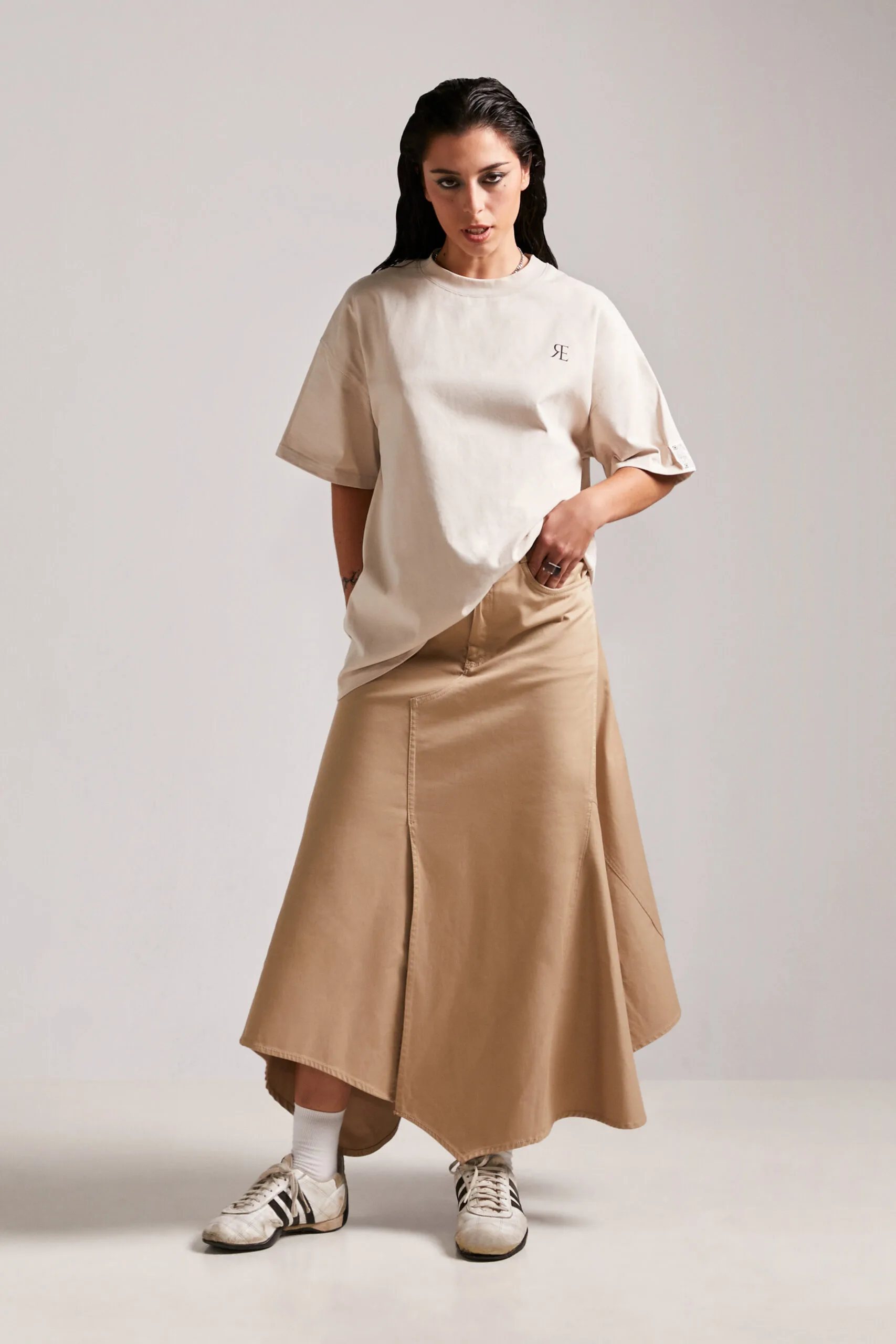 Modelo femenina con camiseta streetwear unisex First Rule Tee y falda asimétrica, una propuesta innovadora de streetwear sostenible.