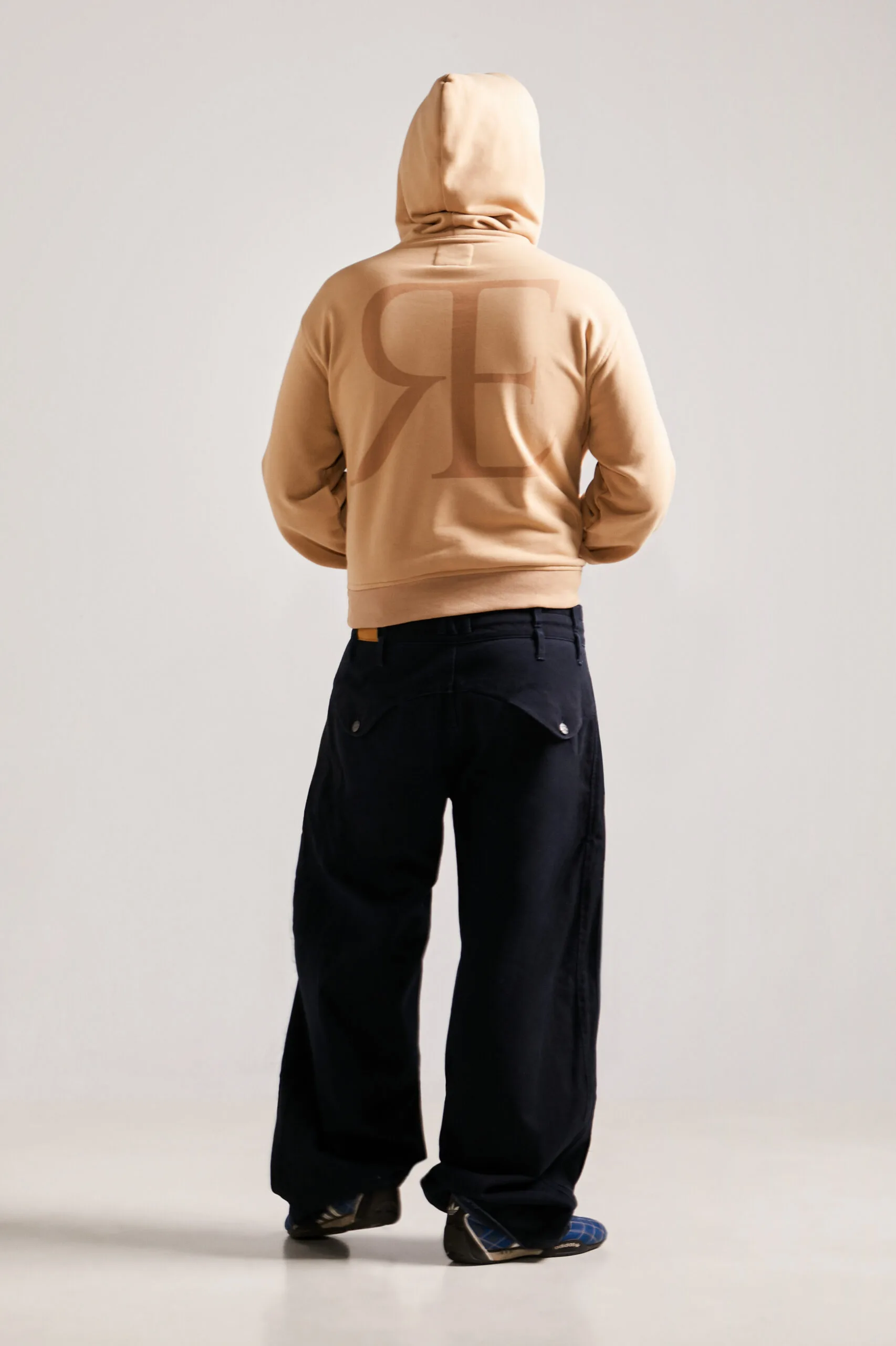 Lookbook trasero de la sudadera Utility Hoodie streetwear unisex beige con el isotipo gigante RE, una pieza icónica de ropa streetwear de lujo.